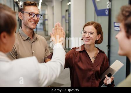 Portrait eines modernen Business-Teams mit hohem Fiving im Büro mit Fokus auf lächelnde Frau mit Tattoos Stockfoto