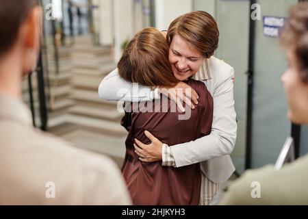 Porträt einer lächelnden Managerin, die eine Mitarbeiterin umarmt und gleichzeitig eine Beförderung im Büro feiert Stockfoto