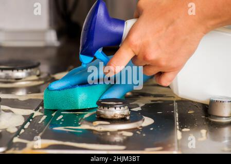Weibliche Hand Reinigung Gasherd mit Schwamm und Reinigungsmittel. Reinigung eines Gasherd mit Küchenutensilien, Haushaltskonzepten oder Hygiene und Reinigung. Stockfoto