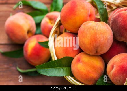 Frisch gepflückte Pfirsiche im Korb auf braunem Holzhintergrund. Reife Pfirsiche im Korb auf Holztisch. Stockfoto