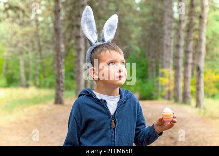 Ein Kind auf der Suche nach Ostereiern im Wald. Kleiner Junge auf der Suche nach Osterei im Frühlingsholz am Ostertag. Das Konzept der Ostereiersuche. Stockfoto