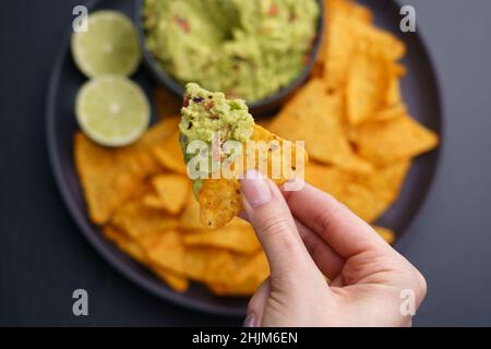 Nahaufnahme der Frauenhand mit Tortilla-Chips oder Nachos mit frischem, schmackhaftem Guacamole-Dip Stockfoto