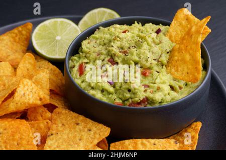 Guacamole Dip mit Tortilla Chips oder Nachos in schwarzer Platte auf schwarzem Hintergrund Stockfoto