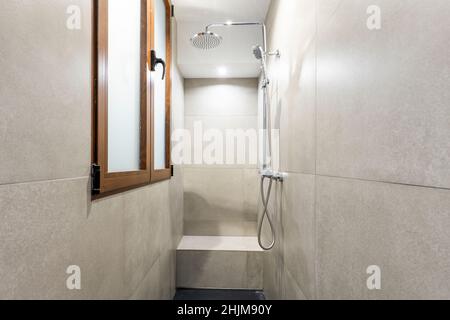 Dusche mit gemauerter Bank, gefliest mit großen grauen Fliesen und holzgerahmten Fenstern Stockfoto