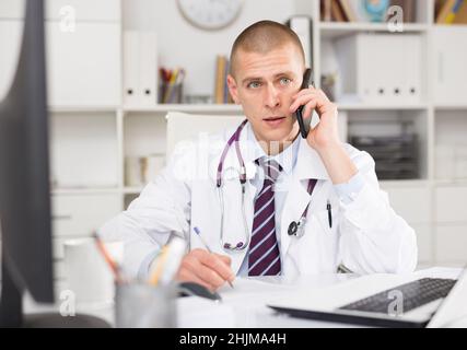 Ein Arzt konsultiert einen Patienten am Telefon im Büro Stockfoto