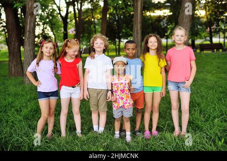 Eine Gruppe von Vorschulkinder verschiedener Rassen umarmen und lächeln vor dem Hintergrund von Grün und einem Park. Kinderschutztag. Stockfoto