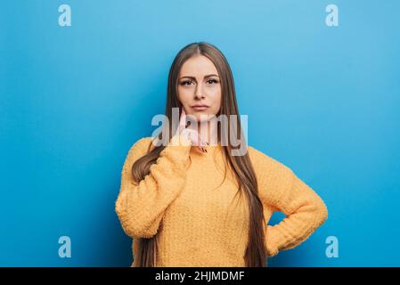 Junge schöne blonde kaukasische Frau mit der Hand in der Nähe des Gesichts und denken. Porträt des weiblichen taktilen Kinns, Traum, träumen mit Zweifeln. Stockfoto