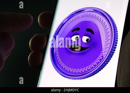 McDonalds Grimace Coin auf dem Smartphone-Bildschirm gesehen in den Händen halten. Gefälschte Meme-Münze. Stafford, Großbritannien, 30. Januar 2022. Stockfoto