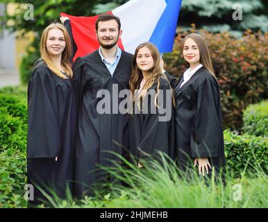 Gruppe von Studenten Absolventen der Fakultät für Fremdsprachen in Roben halten die Flagge Frankreichs in ihren Händen Stockfoto
