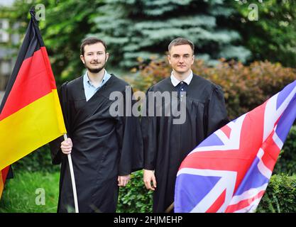 Zwei junge Studenten der Fakultät für Fremdsprachen in Gewändern halten die Fahnen Deutschlands und Großbritanniens in den Händen Stockfoto