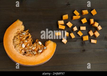 Frischer Bio-Kürbis in Scheiben geschnitten und auf einem dunklen Holztisch gewürfelt Stockfoto