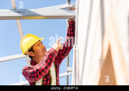 Bauarbeiter oder Bauunternehmer, der den Hausrahmen überprüft, Arbeiter Dachdecker, der auf der Baustelle an einer Stahldachkonstruktion arbeitet Stockfoto