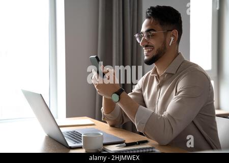 Junger glücklicher Geschäftsmann lächelt beim Lesen und Beantworten der Nachricht auf dem Smartphone Stockfoto