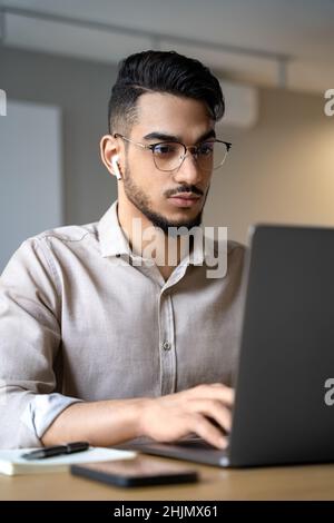 Headshot des jungen ernsthaften indischen Mannes, der online am Laptop-Bildschirm arbeitet Stockfoto