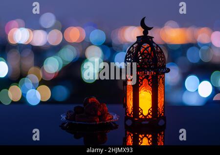 Selektiver Fokus der Laterne, die Mond-Symbol auf der Oberseite und kleine Teller mit Datteln Frucht mit Stadt Bokeh hellen Hintergrund für das muslimische Fest der ho haben Stockfoto