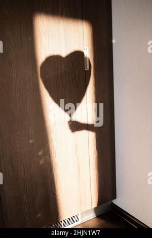 Romantik und Einsamkeit im Stadtschatten der Hand eines Mannes, der einen herzförmigen Ballon hält. Silhouette an der Wand. Suche nach Liebe Konzept, Stockfoto