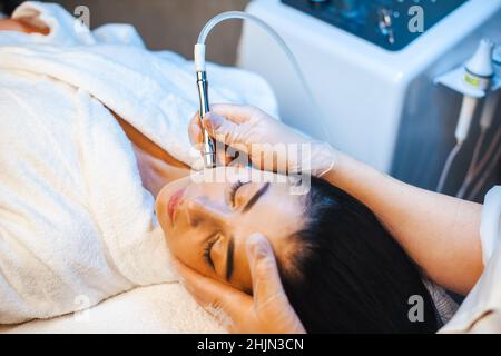 Nahaufnahme eines Porträts der Hände des Kosmetikers, die Mikrodermabrasion auf dem Gesicht einer Frau in einem Schönheitssalon durchführen. Gesichtshautbehandlung Stockfoto