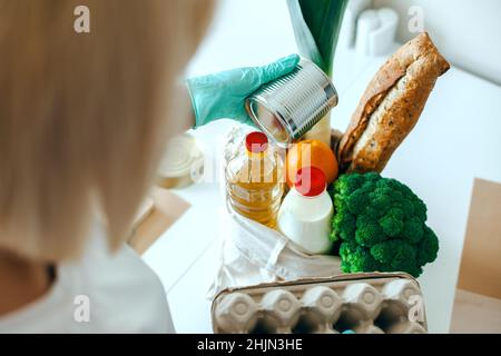 Hände des Freiwilligen in Handschuhe, die Nahrung in eine Spendenverpackung stecken. Hände, die Spenden zubereiten. Virenschutz. Stockfoto