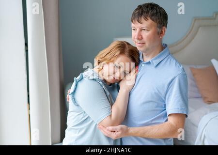 Verträumte Paar Familie Verbindung Kuscheln Blick in die Ferne durch Fenster. Liebevolle Hausbesitzer, Mann und Frau, visualisieren eine gemeinsame Zukunft und genießen einen Neuanfang drinnen zusammen. Stockfoto