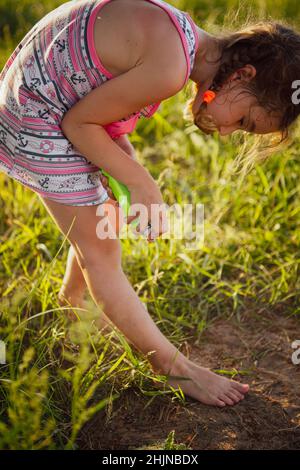 Mädchen sprüht Mückenspray auf die Haut in der Natur, die ihre Hände und Füße beißen. Schutz vor Insektenstichen, abweisend sicher für Kinder. Außenrekr Stockfoto
