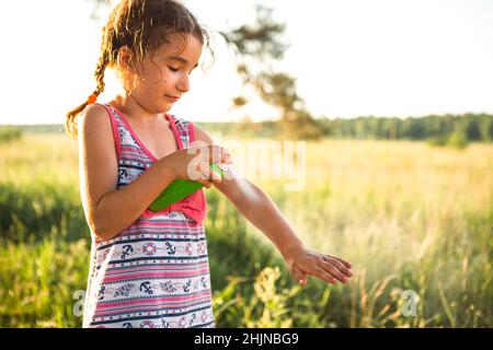 Mädchen sprüht Mückenspray auf die Haut in der Natur, die ihre Hände und Füße beißen. Schutz vor Insektenstichen, abweisend sicher für Kinder. Außenrekr Stockfoto