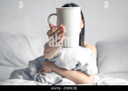 Eine Frau hält eine Tasse Kaffee, während sie im Bett liegt. Stockfoto