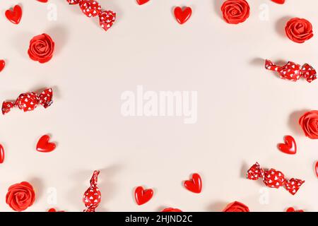 Süßigkeiten zum Valentinstag, herzförmige Konfetti und rote Rosen bilden einen Rahmen um beigen Hintergrund mit Kopierraum Stockfoto