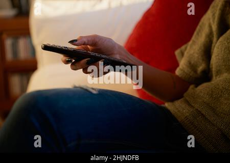 Hand einer multikulturellen jungen erwachsenen Frau mit Fernbedienung für den Fernseher. Moderne Wohnung, bequem auf dem Sofa sitzen Stockfoto