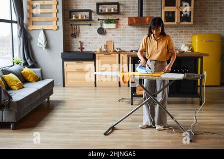 Porträt einer jungen Frau, die zu Hause Kleidung bügelt und am Wochenende Hausaufgaben macht, Platz kopieren Stockfoto