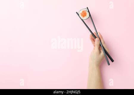 Weibliche Hand hält Sushi mit Essstäbchen auf rosa Hintergrund Stockfoto