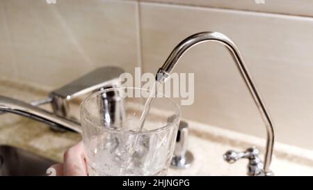 Wasser wird aus dem Küchenhahn in das Glas gegossen. Konzept. Nahaufnahme von Leitungswasser, das in ein Glas in der Küche gegossen wird. Stockfoto
