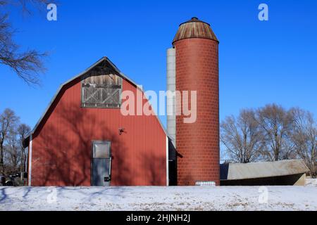 Ein Red Barn und Silo mit Schnee im Winter mit blauem Himmel in Kansas Stockfoto