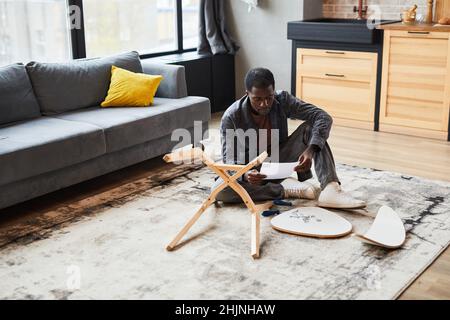 Weitwinkelporträt eines jungen afroamerikanischen Mannes, der zu Hause Möbel zusammenstellt und Platz kopiert Stockfoto