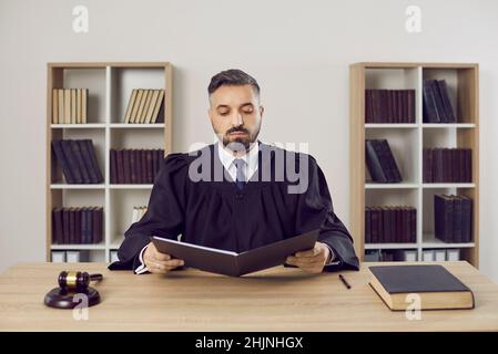 Seriöse männliche Richter liest rechtliche Dokumente auf Fall sitzen am Tisch in seinem Büro. Stockfoto