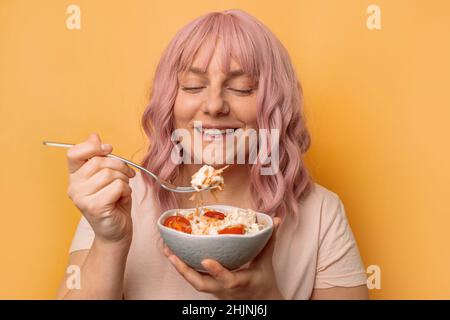 Fröhliche junge glückliche Frau, die gesunden Gemüsesalat auf gelbem Hintergrund isst. Fitness und gesundes Lifestyle-Konzept. Stockfoto