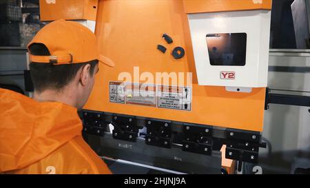 Arbeiter in der Fabrik bei Metal skip Maschine, die das Werkstück einlegt. Clip. Mann, der mit Blech und speziellen Werkzeugmaschinen zum Biegen arbeitet. Stockfoto