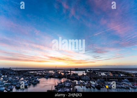 Farbenprächtiger Morgenhimmel über dem Ärmelkanal und dem Ramsgate Royal Harbour in Kent, England. Hafen gefüllt mit Booten und einem Yachthafen mit einem Himmel über Cirrus fibratus Wolken.Rosa rote Wolken und gelber Himmel ändern sich zu blau höher. Stockfoto