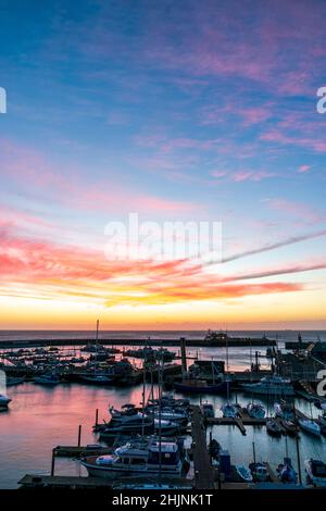 Farbenprächtiger Morgenhimmel über dem Ärmelkanal und dem Ramsgate Royal Harbour in Kent, England. Der Hafen ist voll mit Booten und einem Jachthafen mit einem Himmel über dem Himmel aus roten, rosafarbenen Wolken und einem gelben Himmel, der höher in Blau wechselt. Stockfoto