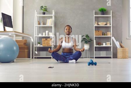 Junge afroamerikanische Frau zu Hause, die Meditation praktiziert und in Lotusposition sitzt. Stockfoto