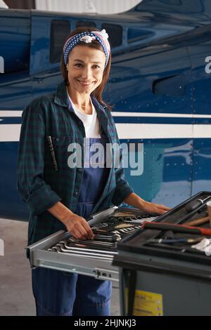 Ingenieurin mit niedlichem Lächeln in Uniform, die in der Nähe des Privatflugzeugs arbeitet Stockfoto