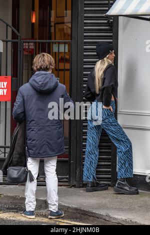 Ein junges Mädchen mit langen blonden Haaren und einem warmen Hut auf dem Kopf posiert für ein Foto für ihre Freundin, Stadt- und Straßenfotografie, Dublin, Irland Stockfoto