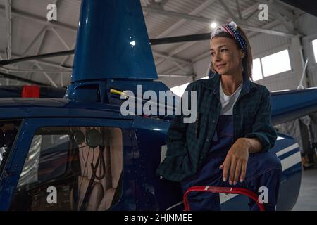 Charmante Mechanikerin posiert an der Fotokamera in der Nähe des Kopters im Hangar Stockfoto