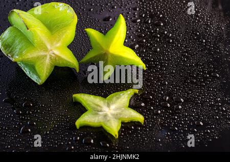 Frischer Karambol auf schwarzem Hintergrund mit Tropfen Stockfoto