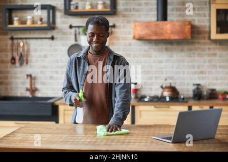 Porträt eines lächelnden afroamerikanischen Mannes, der die Frühjahrsputz in einem modernen Zuhause genießt, Kopierraum Stockfoto