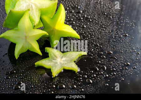 Frischer Karambol auf schwarzem Hintergrund mit Tropfen Stockfoto