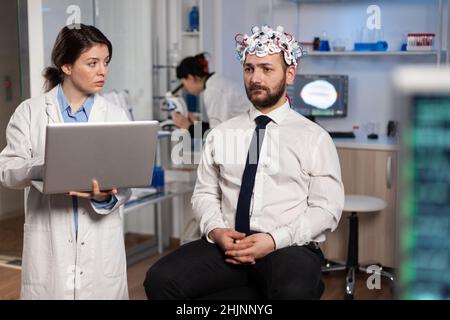 Forscherin Ärztin, die neurologische Krankheitssymptome auf dem Laptop eingibt, um die medizinische Behandlung mit dem Patienten zu besprechen. Neurologe überwacht die Aktivität des Nervensystems des Menschen mit eeg-Headset Stockfoto