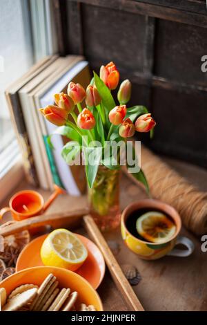 Stillleben auf dem Tisch. Bouquet von roten Tulpen und Tee mit Zitrone in einer Tasse. Vase. Stockfoto