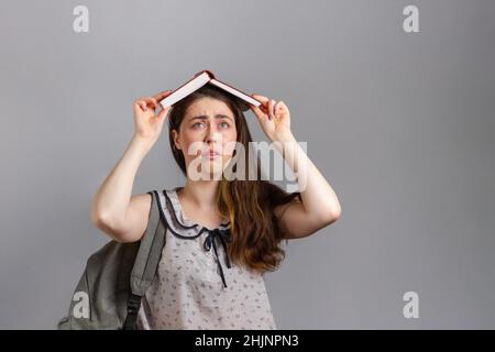 Bildung. Eine junge Frau oder ein Teenager mit einem Rucksack auf dem Rücken, machte das Dach des Hauses aus einem Buch, über ihren Kopf.die Emotion der Unzufriedenheit. C Stockfoto