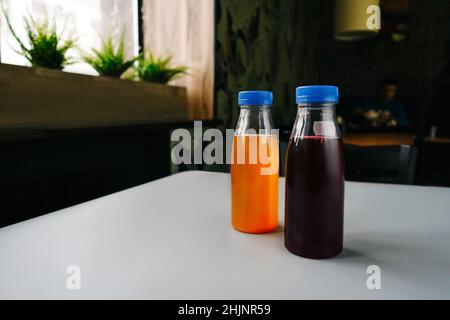 Plastikflaschen mit Obst- oder Gemüsesäften auf grauem Tisch im Hintergrund des Cafés. Stockfoto