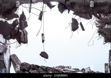 Ein Loch im Körper eines Gebäudes mit einem Haufen Bauschutt und Betonfragmenten, die an der Stange an einem einheitlichen grauen Himmel hängen. Hintergrund Stockfoto